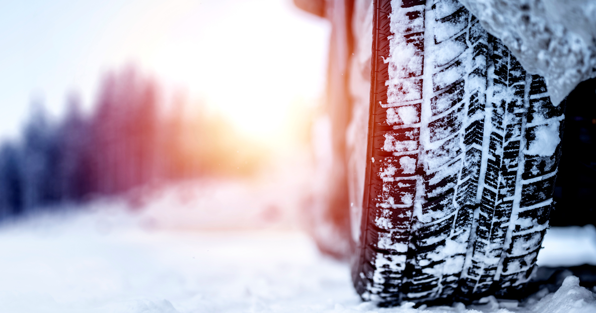 Close-up of a tire covered in snow with a snowy landscape blurred in the background